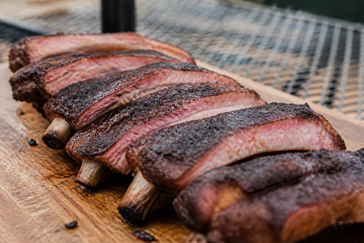 Sliced pork ribs on a wooden board with a visible smoke ring