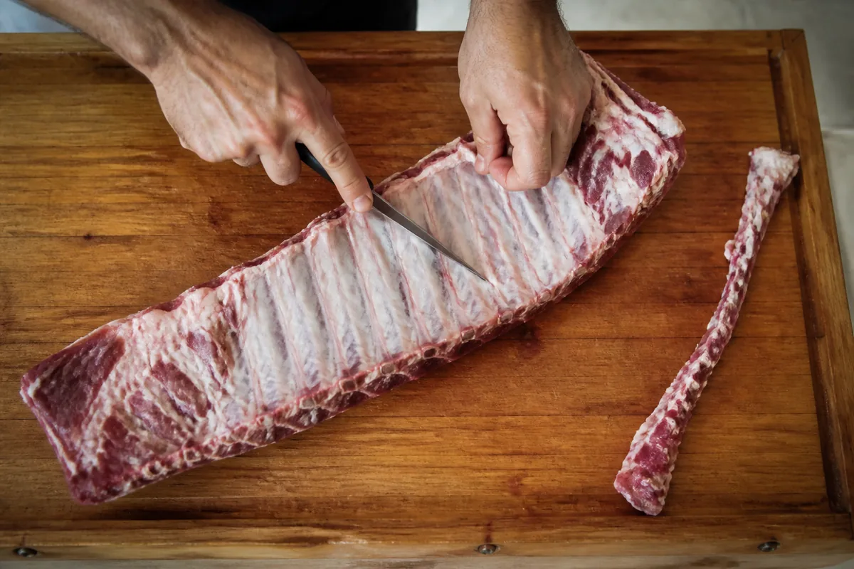 Hands trimming a rack of spare ribs with a boning knife